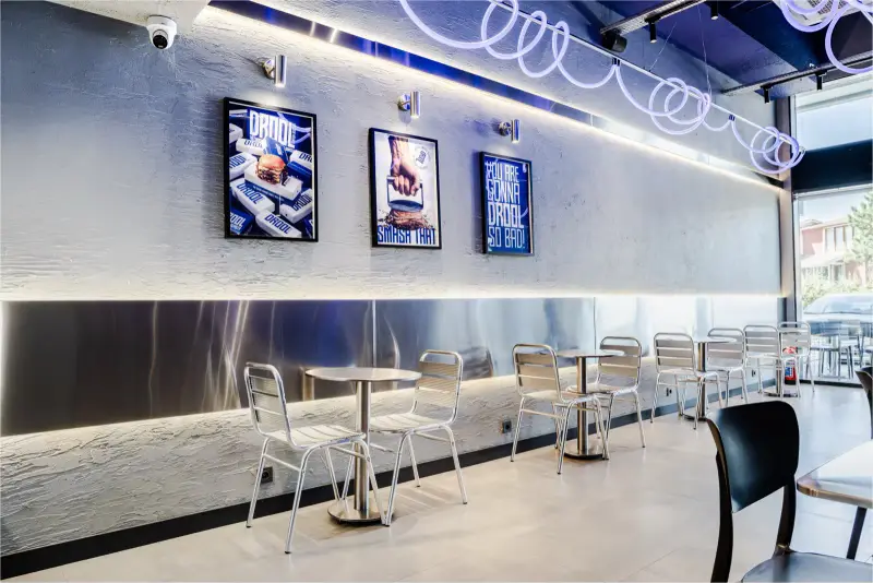 Çerçeveli marka posterleri ve neon halka aydınlatmalı oturma alanı fotoğrafı, Droll Smash Burger için Ankara mimari fotoğrafçısı Şems Erik.