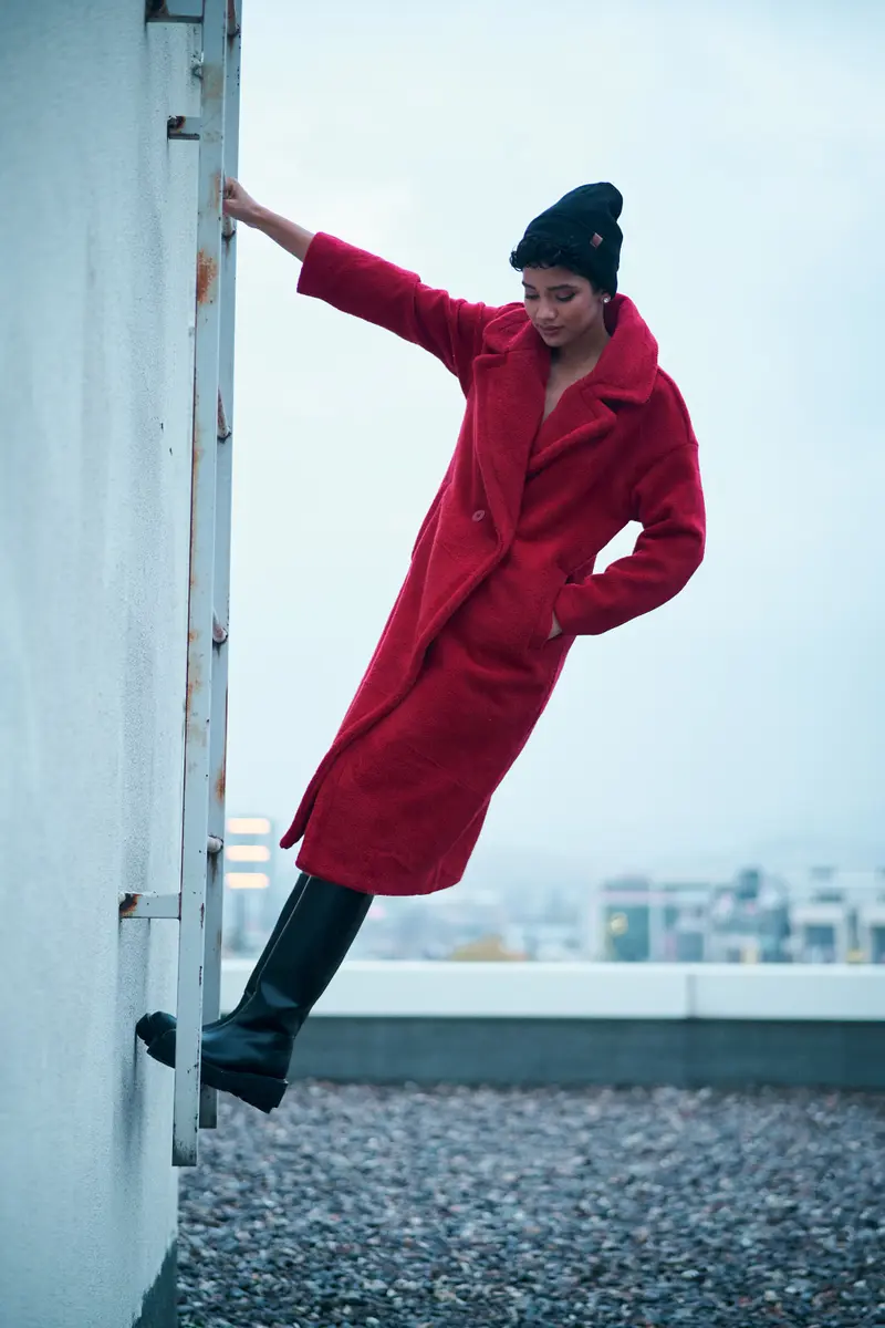 Kırmızı kabanlı ve bereli model Taahira çatı merdivenine tutunmuş, aşağı bakıyor, hareketli moda fotoğrafı, Ankara moda fotoğrafçısı Şems Erik.