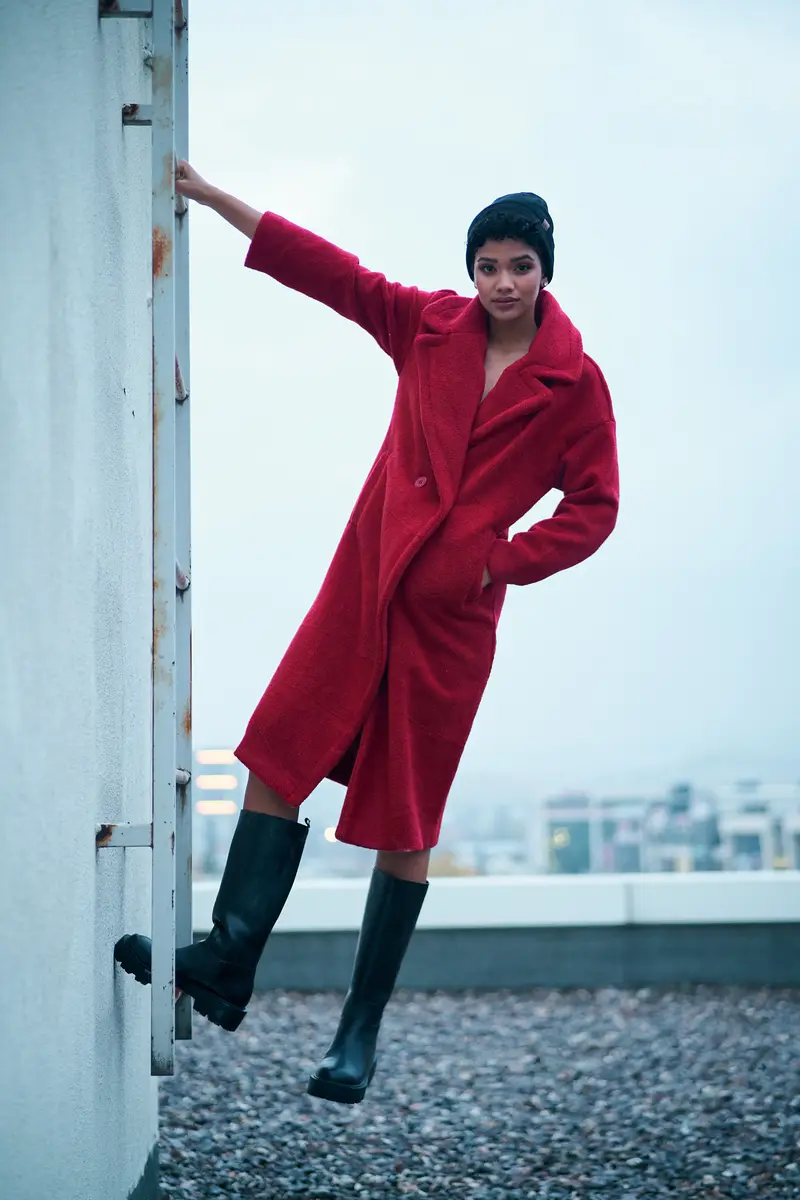 Kırmızı kabanlı model Taahira çatı merdivenine tutunarak kameraya bakıyor, siyah çizmeleriyle havada, moda fotoğrafı, Ankara moda fotoğrafçısı Şems Erik.